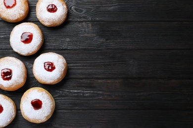 Hanukkah doughnuts with jelly and sugar powder on black wooden table, flat lay. Space for text