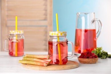 Tasty rhubarb cocktail with raspberry and stalks on white wooden table