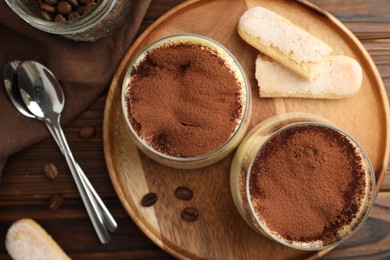 Photo of Delicious tiramisu in glasses served on wooden table, flat lay