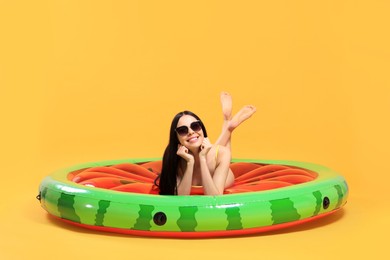 Happy young woman with beautiful suntan and sunglasses on inflatable mattress against orange background