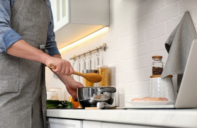 Man making dinner while watching online cooking course via laptop in kitchen, closeup