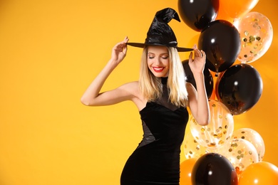 Photo of Beautiful woman in witch costume with balloons on yellow background, space for text. Halloween party