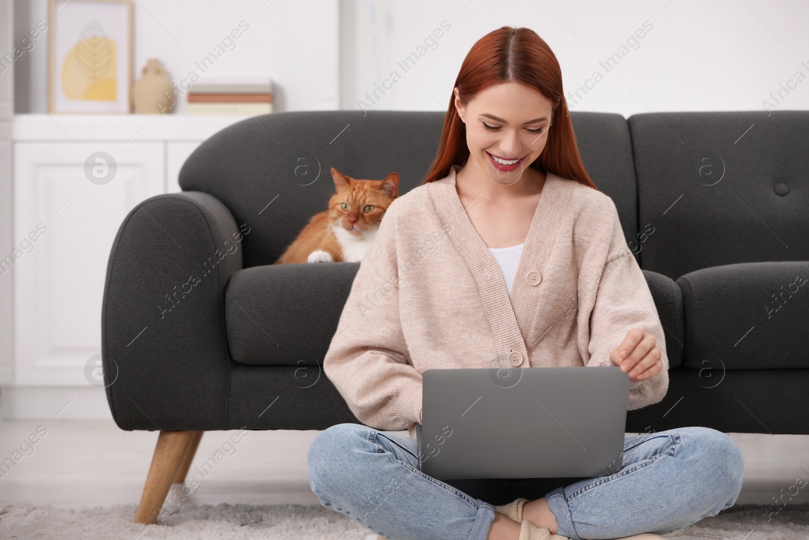 Photo of Happy woman working with laptop near cat on sofa at home