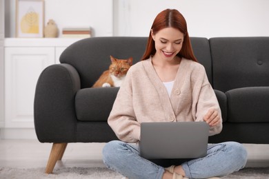 Photo of Happy woman working with laptop near cat on sofa at home
