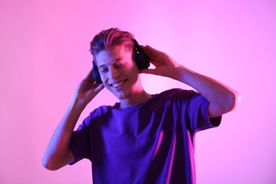 Young man with headphones on pink background in neon lights