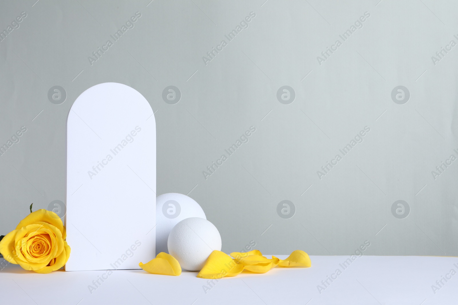 Photo of Beautiful presentation for product. Geometric figures and yellow rose on white table against light grey background, space for text