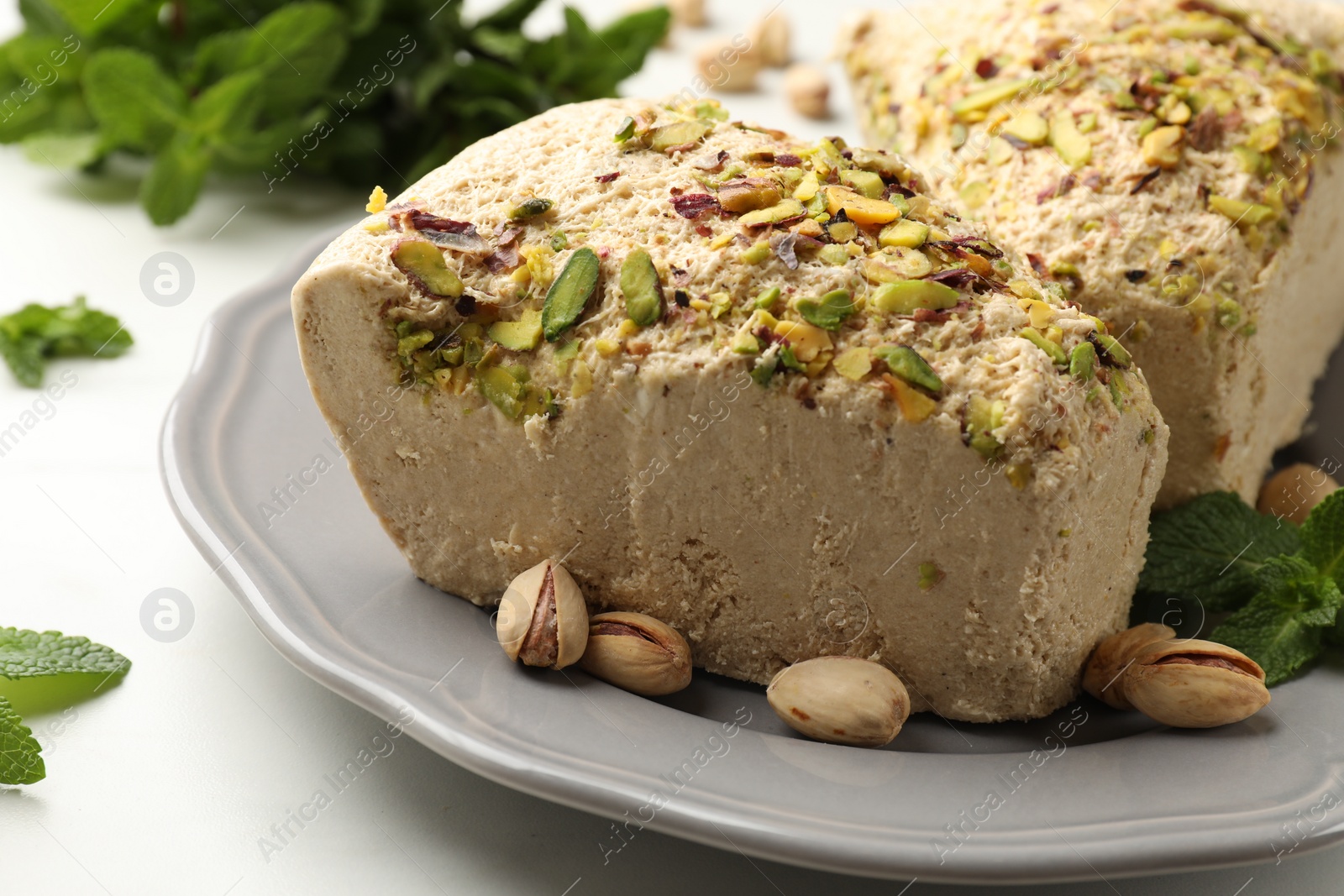 Photo of Pieces of tasty halva with pistachios and mint on table, closeup