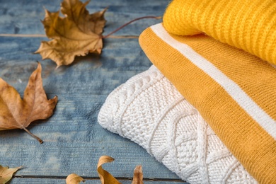 Photo of Stack of folded knitted sweaters and autumn leaves on table. Space for text