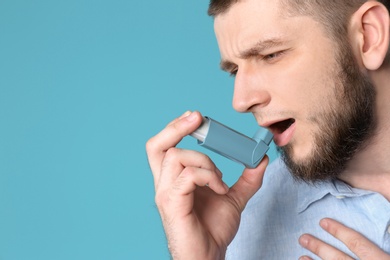 Young man using asthma inhaler on color background