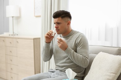 Photo of Ill man with paper tissue using nasal spray at home