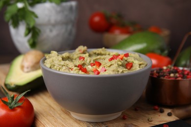 Photo of Bowl of delicious guacamole and ingredients on wooden board, closeup