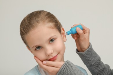 Mother dripping medication into daughter's ear on light grey background