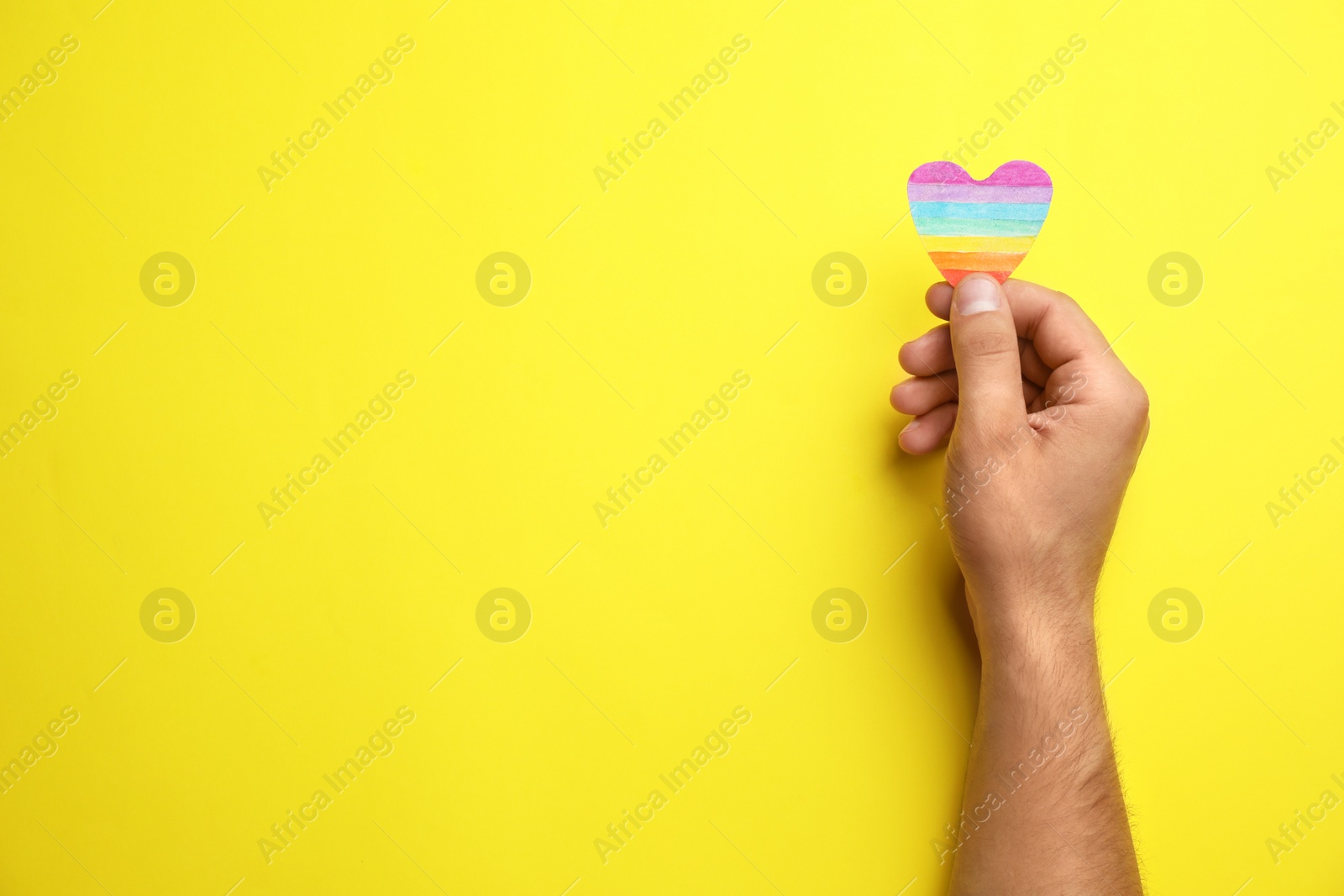 Photo of Man with rainbow heart on yellow background, top view and space for text. Gay symbol