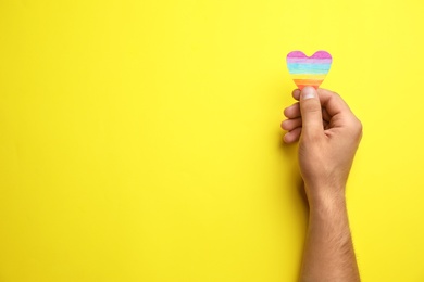 Man with rainbow heart on yellow background, top view and space for text. Gay symbol