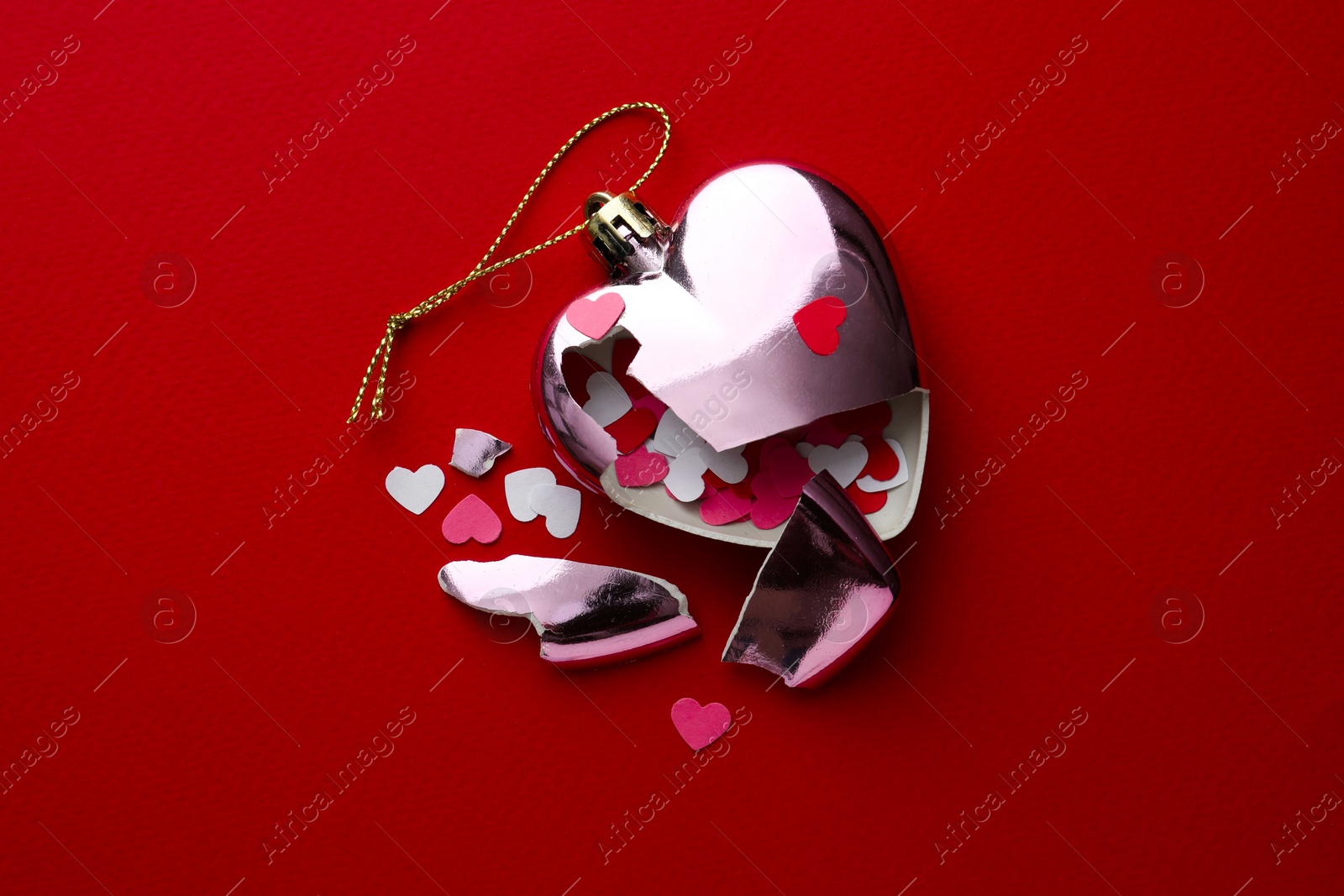 Photo of Crashed bauble in shape of heart with confetti on red background, top view. Broken heart