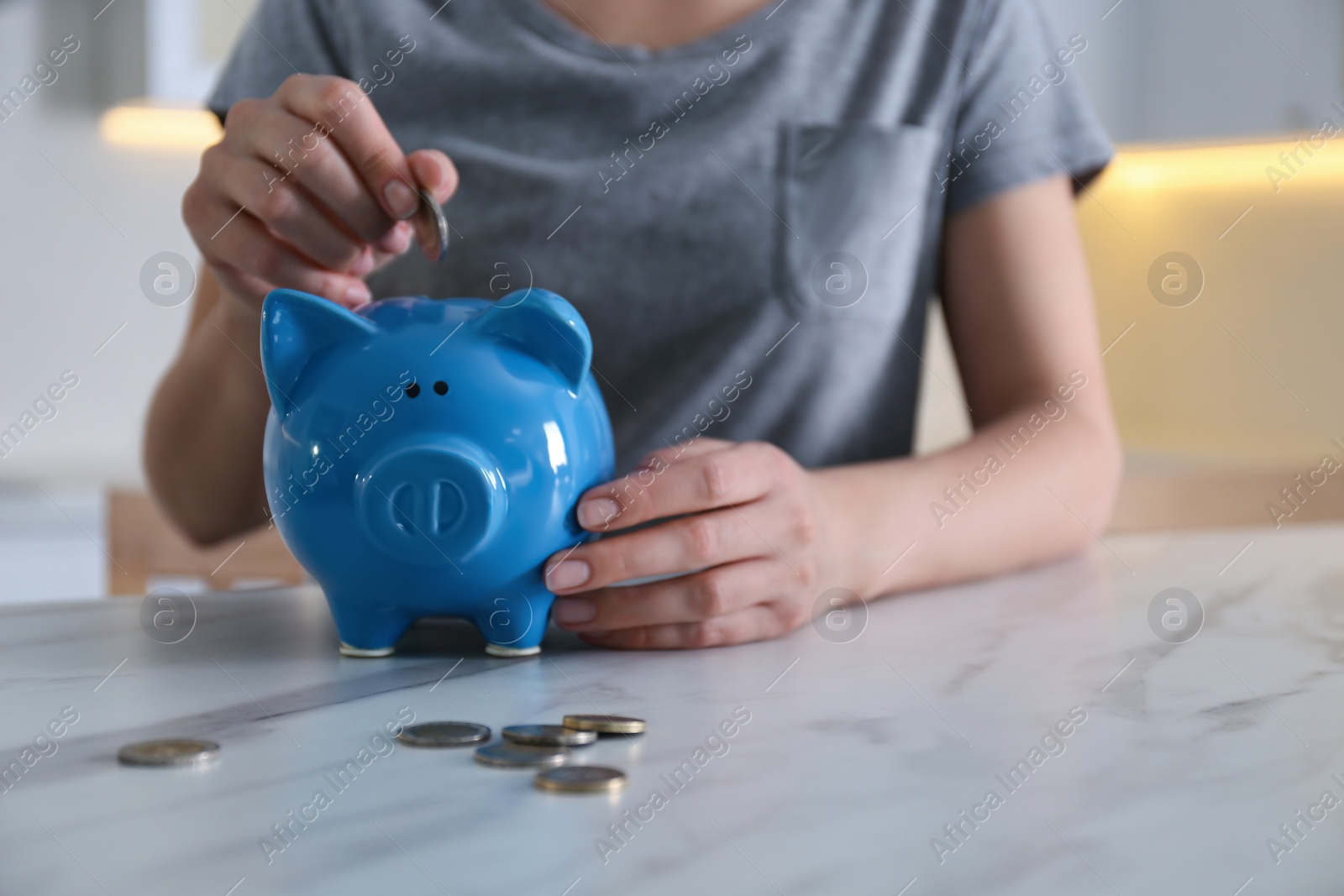 Photo of Woman putting money into piggy bank at marble table indoors, closeup