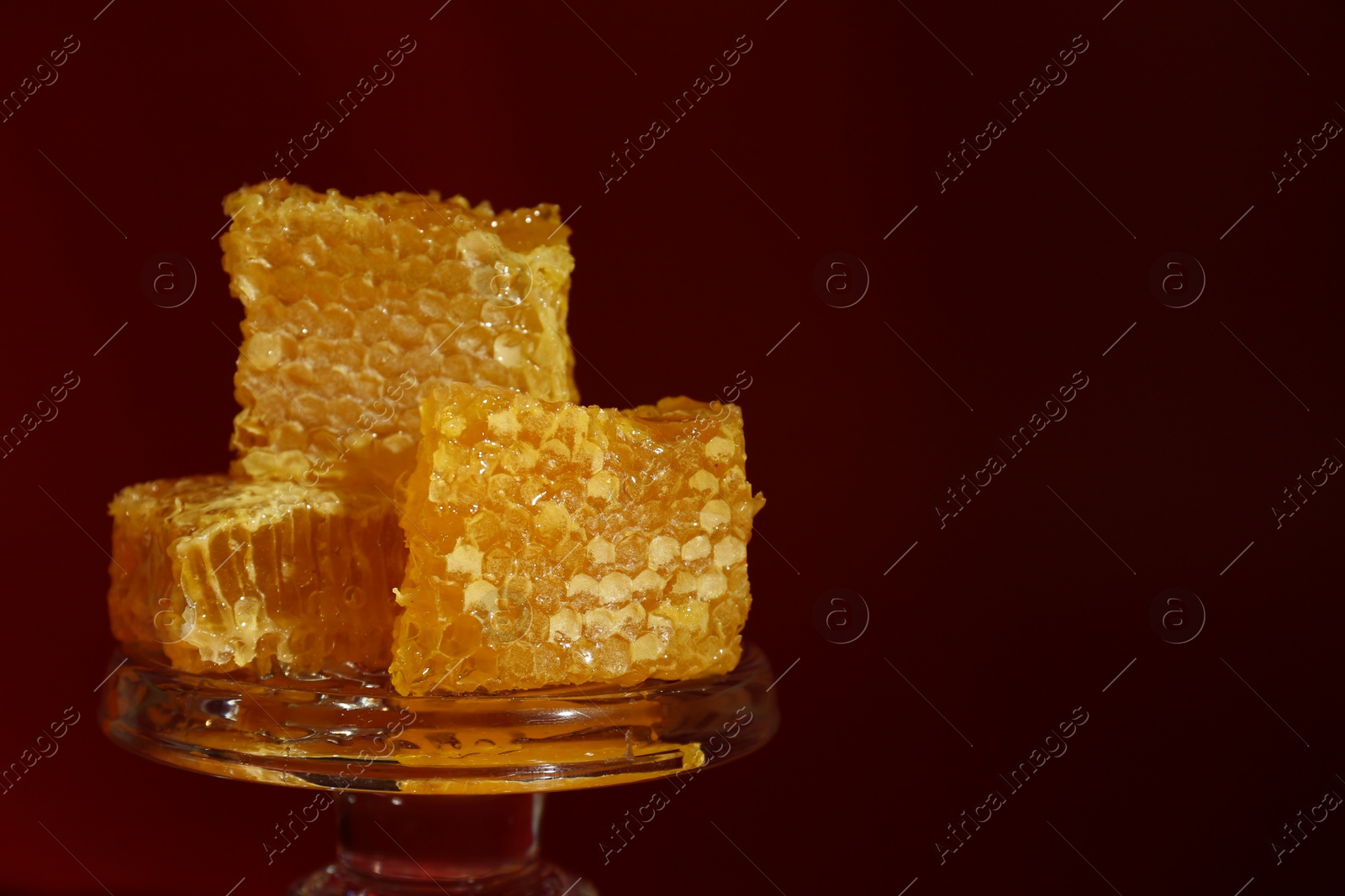 Photo of Natural honeycombs on glass stand against burgundy background, space for text