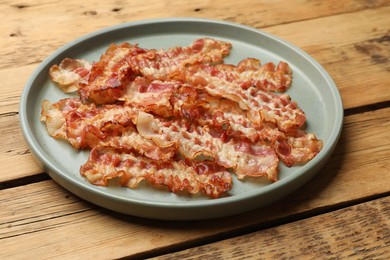 Photo of Delicious fried bacon slices on wooden table