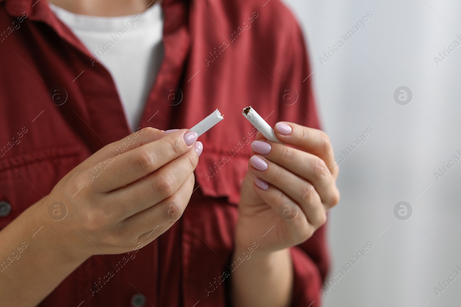 Photo of Stop smoking concept. Woman holding pieces of broken cigarette on light background, closeup