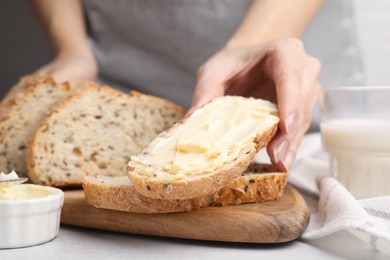 Photo of Woman taking slice of bread with tasty butter at table, closeup