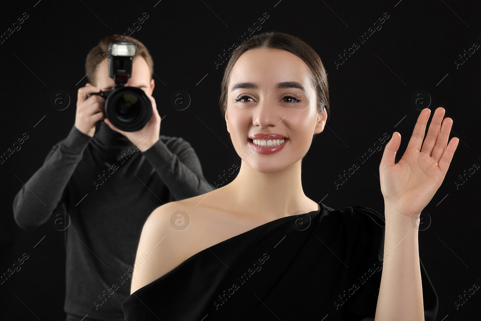 Photo of Photographer taking picture of beautiful woman on black background, selective focus