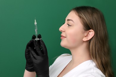 Photo of Cosmetologist in gloves with syringe on green background