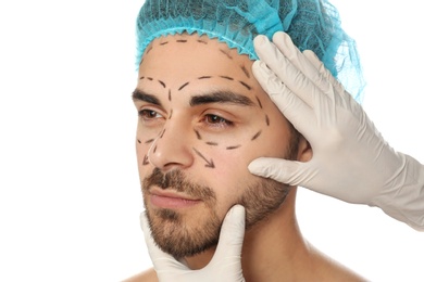 Doctor examining man's face with marker lines for plastic surgery operation on white background