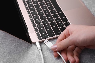 Woman holding plugged USB cable into laptop at grey table, closeup