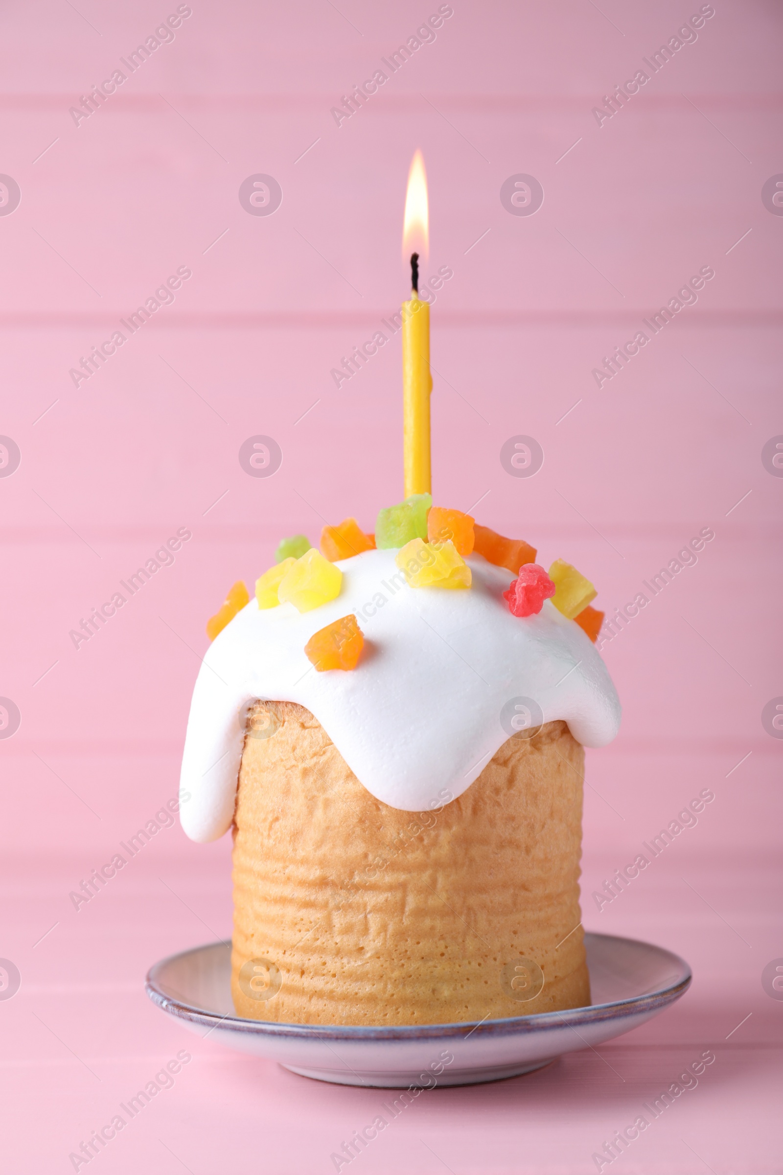 Photo of Easter cake with burning candle on pink wooden table