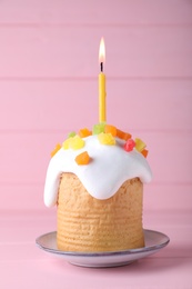 Photo of Easter cake with burning candle on pink wooden table