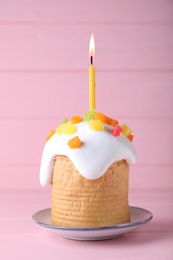 Easter cake with burning candle on pink wooden table