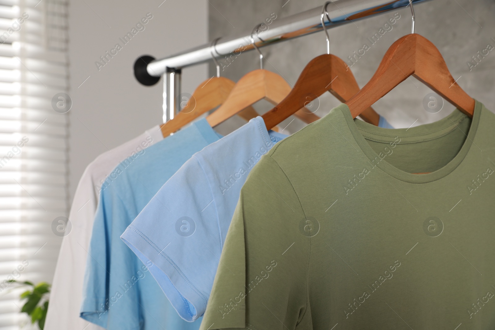 Photo of Clean T-shirts hanging on rack indoors, closeup