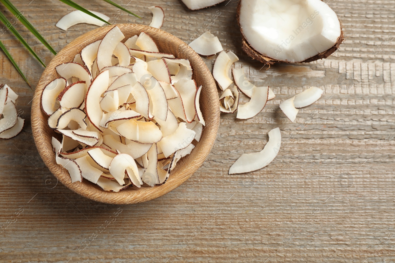 Photo of Tasty coconut chips on wooden table, flat lay