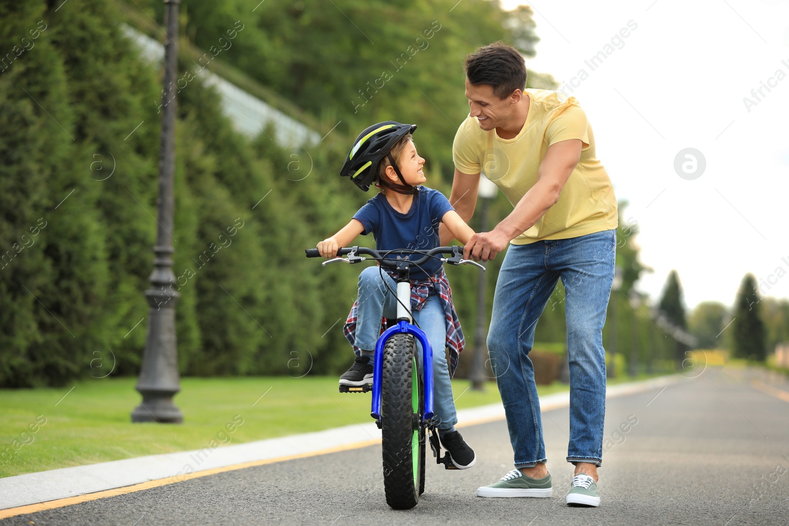 Image of Dad teaching son to ride bicycle outdoors