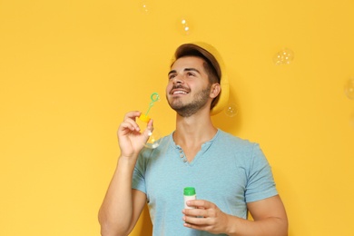 Young man blowing soap bubbles on color background. Space for text
