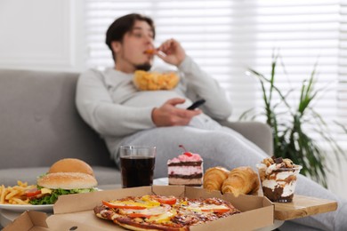 Photo of Overweight man with chips watching TV at home, focus on junk food