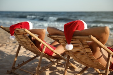 Photo of Lovely couple with Santa hats relaxing on deck chairs at beach. Christmas vacation
