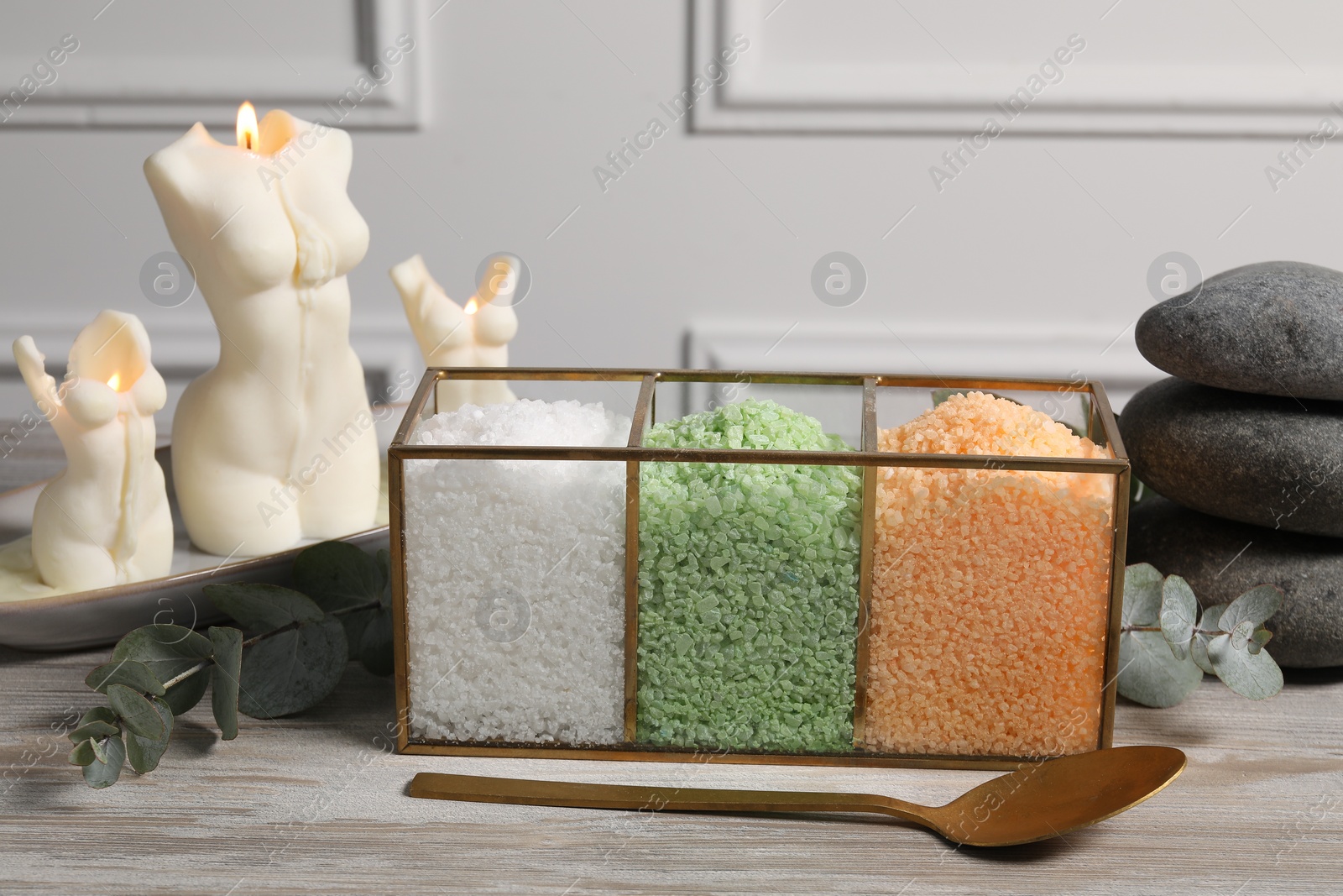 Photo of Different types of sea salt, spoon, spa stones, candles and eucalyptus branches on wooden table