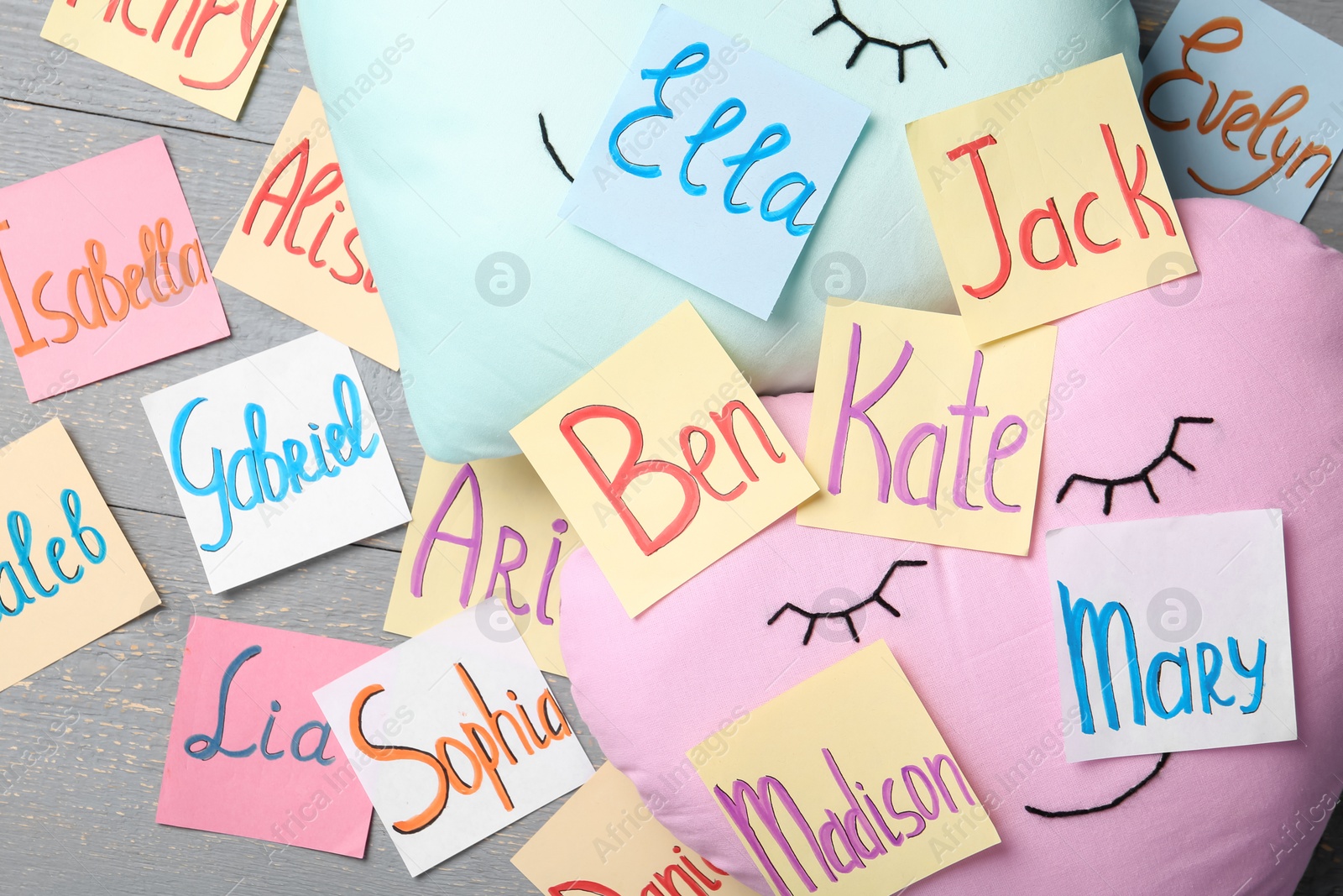 Photo of Colorful paper sheets with written different baby names on grey wooden table, flat lay