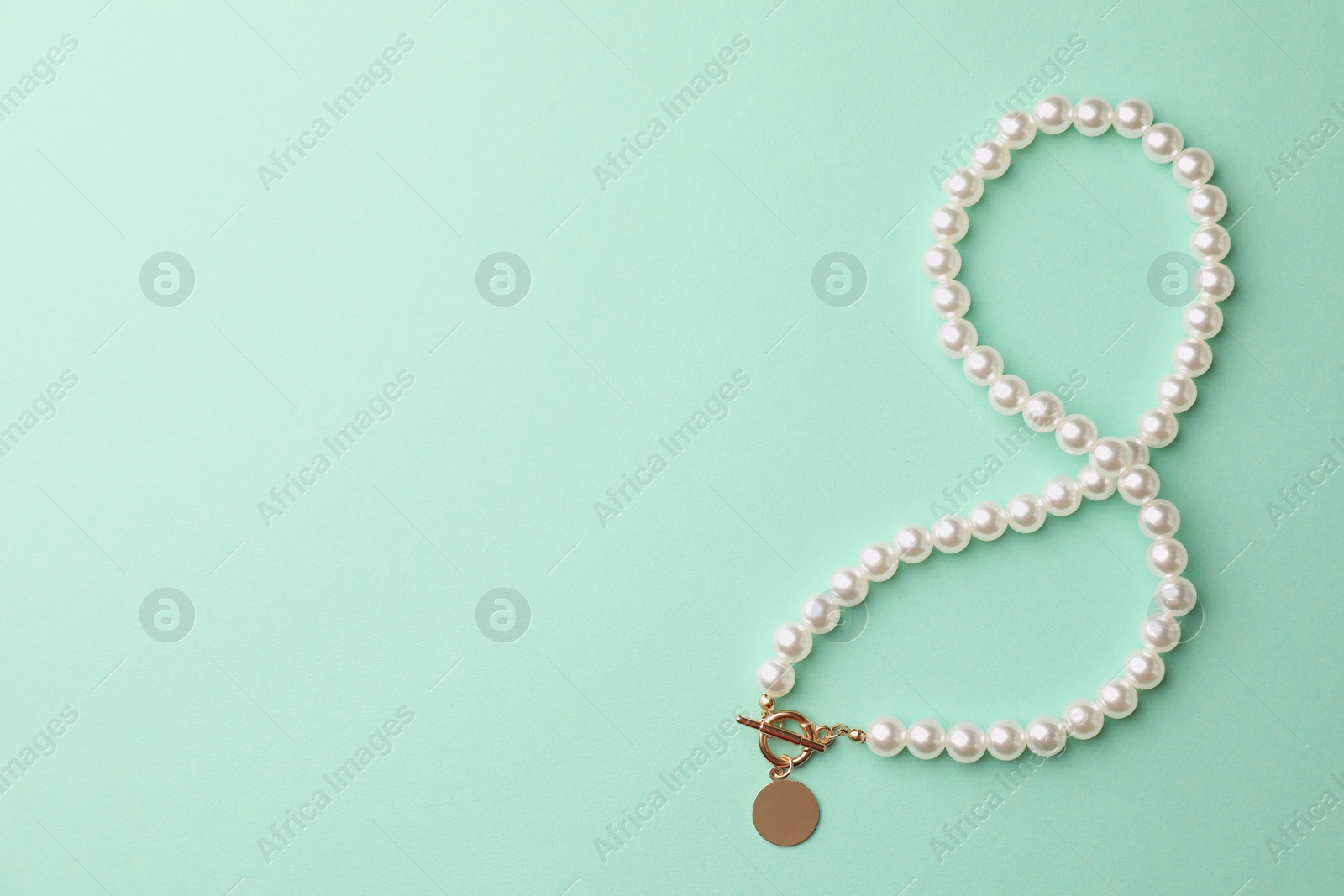 Photo of Elegant pearl necklace on turquoise background, top view. Space for text