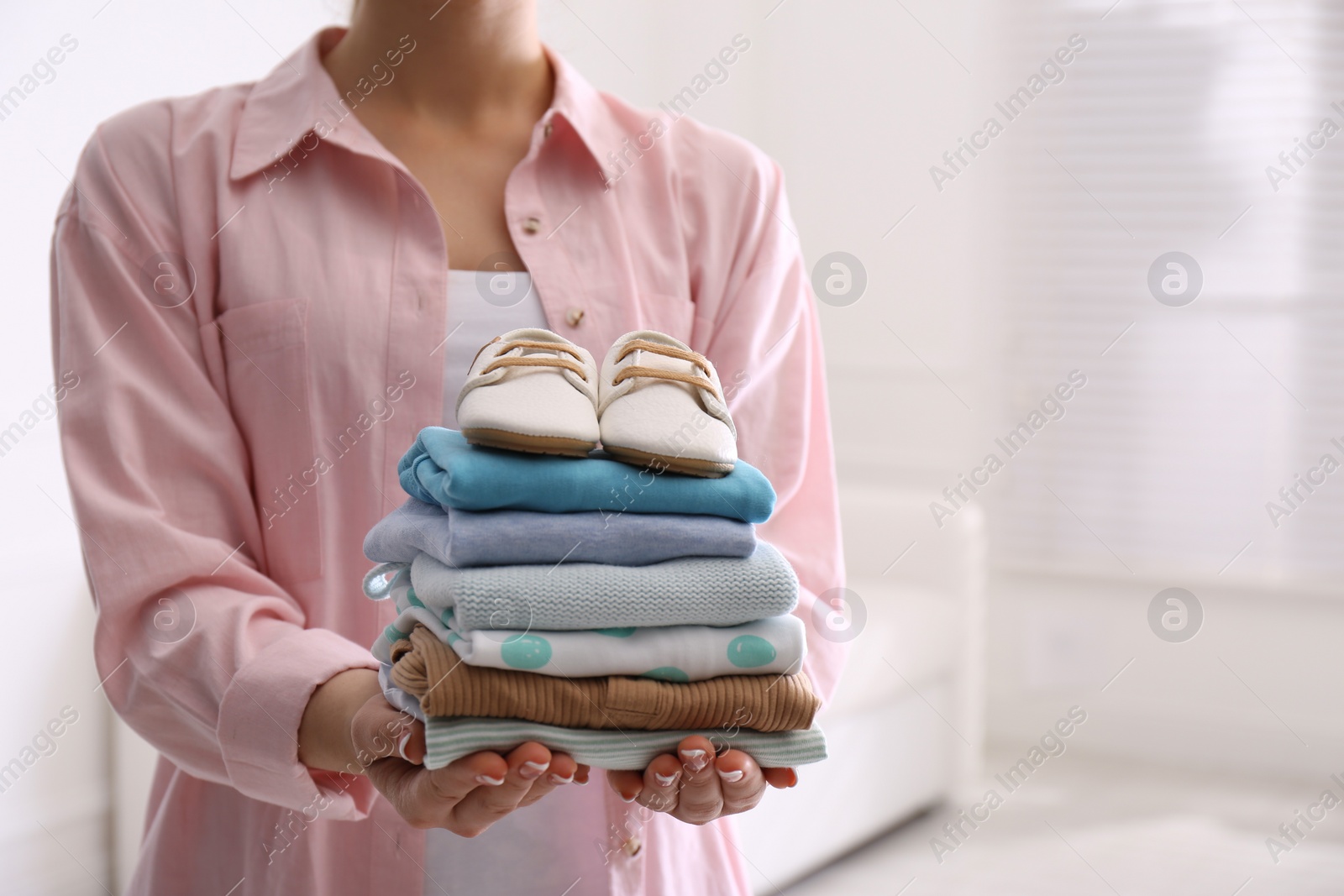 Photo of Woman holding stack of baby's clothes and small shoes indoors, closeup. Space for text