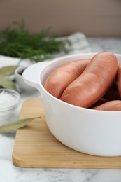 Photo of Bowl of delicious sausages, dill, bay leaf and salt on white marble table
