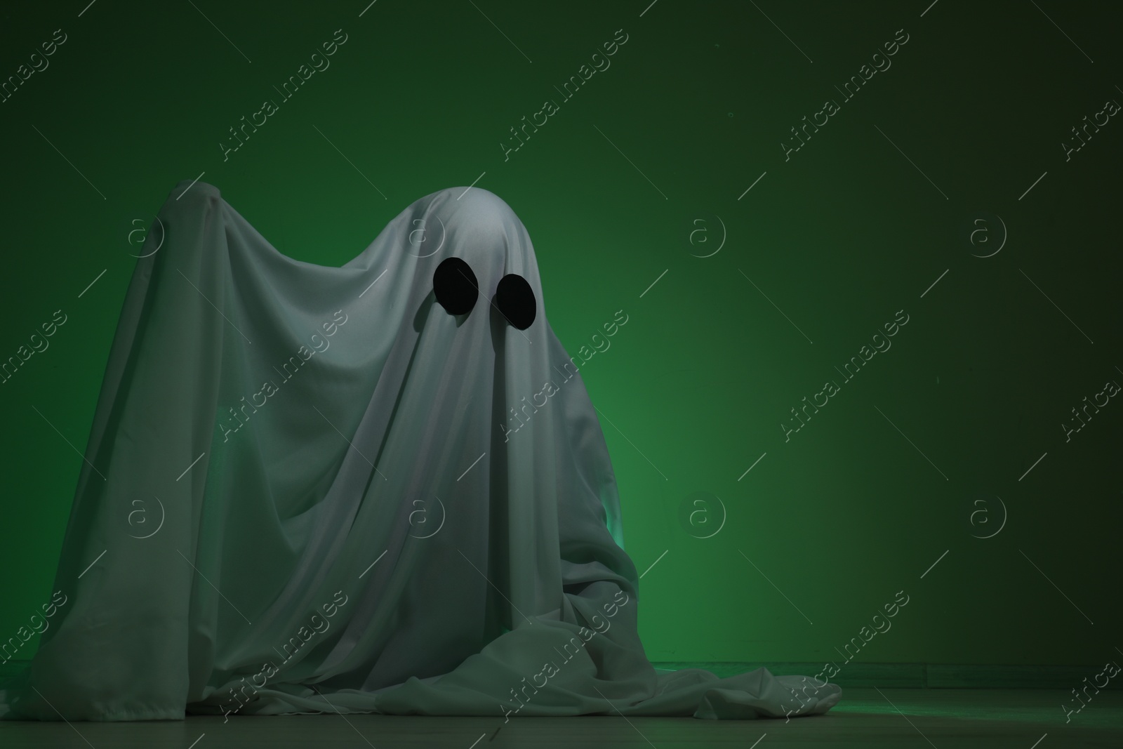 Photo of Creepy ghost. Woman covered with sheet in green light, space for text