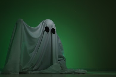 Creepy ghost. Woman covered with sheet in green light, space for text