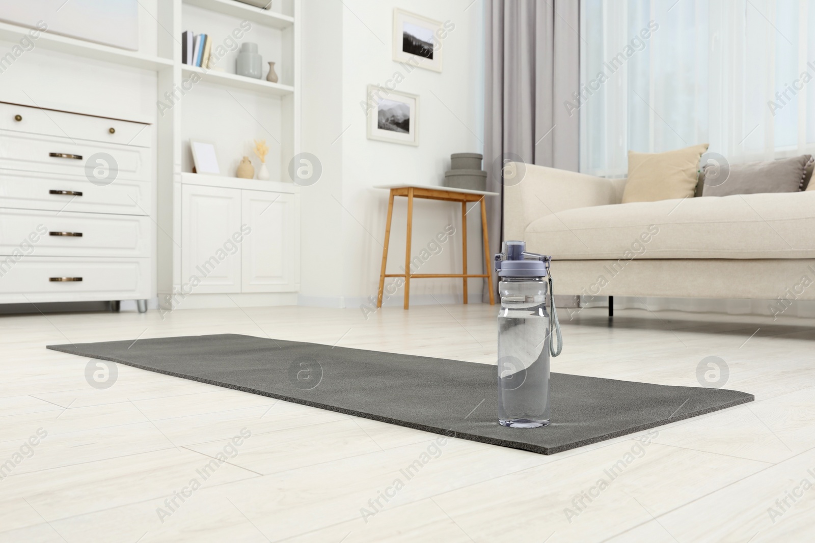 Photo of Yoga mat and bottle of water on floor in room