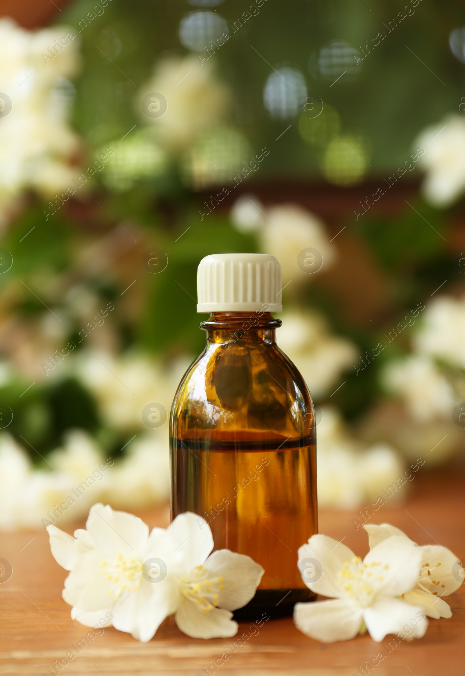 Photo of Bottle of jasmine essential oil and beautiful flowers on wooden table