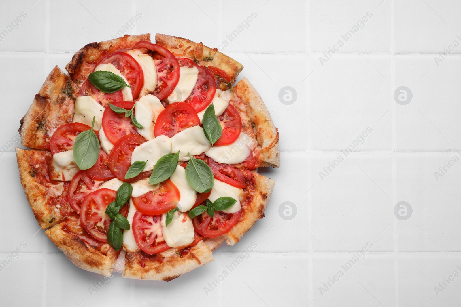 Photo of Delicious Caprese pizza with tomatoes, mozzarella and basil on white tiled table, top view. Space for text