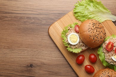 Photo of Delicious sandwiches with tuna, boiled egg and vegetables on wooden table, top view. Space for text