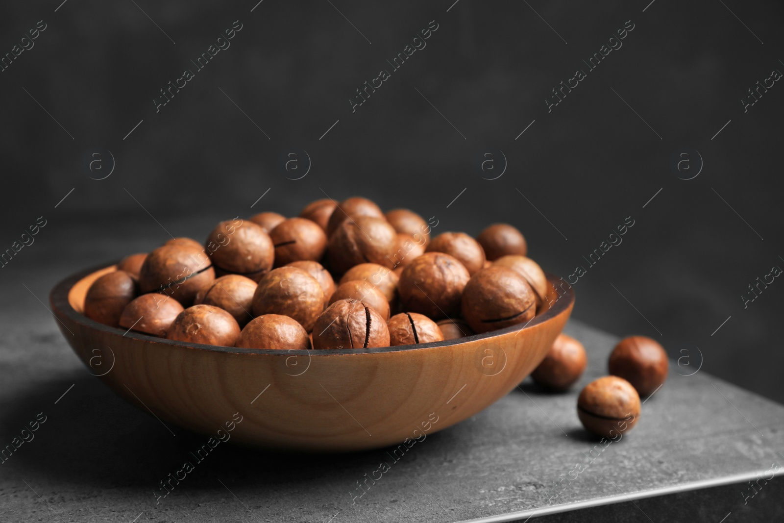 Photo of Plate with organic Macadamia nuts on table against dark background. Space for text