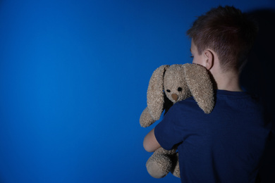 Photo of Sad little boy with toy near blue wall, space for text. Domestic violence concept